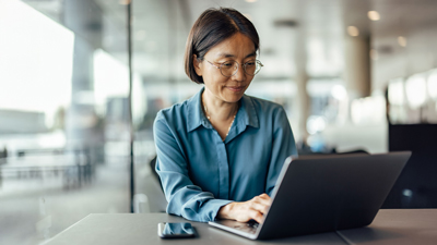 Woman seated in an office setting typing on her laptop.