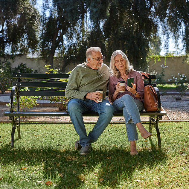 A senior couple outdoors sitting on a park bench. 