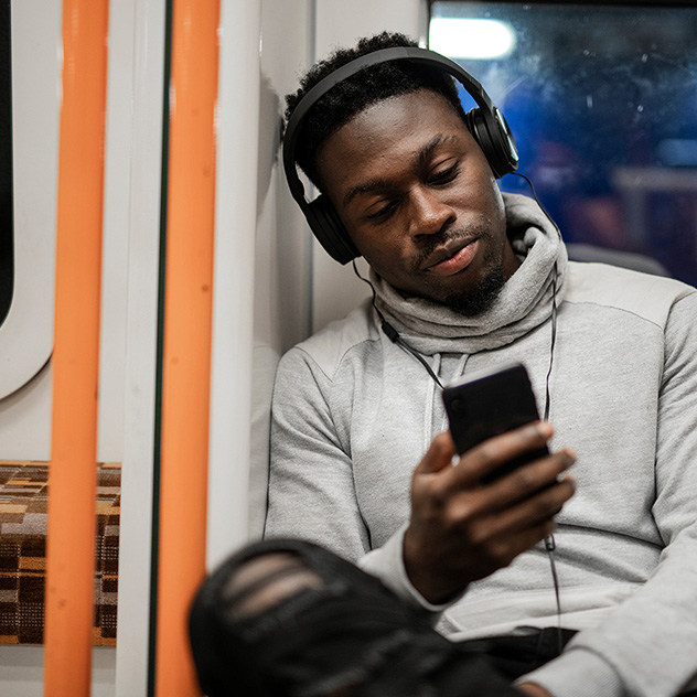 A man on the subway listening to headphones and looking at his smartphone.  